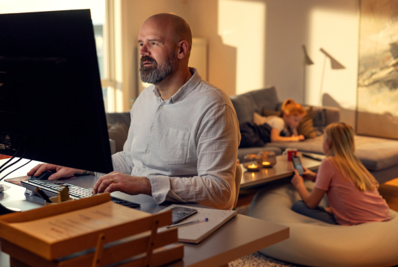 Mann ser på PC i stuen med barna i bakgrunnen
