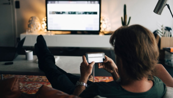 Mann ser på mobil og tv