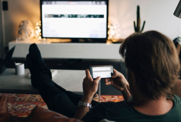 Mann ser på mobil og tv