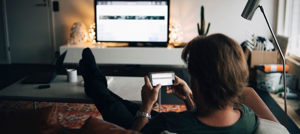 Mann ser på mobil og tv