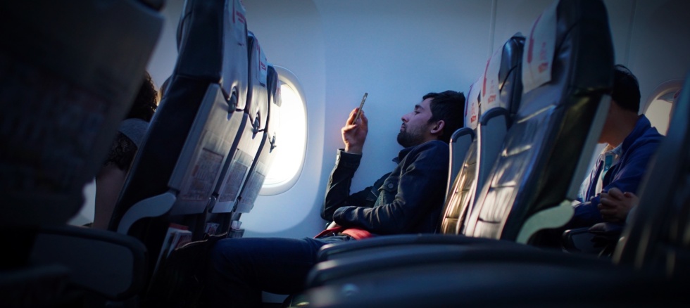 Mann sitter i flysetet og surfer på mobilen