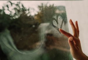 en kvinne lager et hjerte på et regnfullt vindu