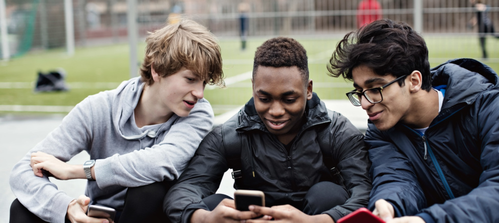 Unge tenåringsgutter som surfer på internett på telefonen på en idrettsplass